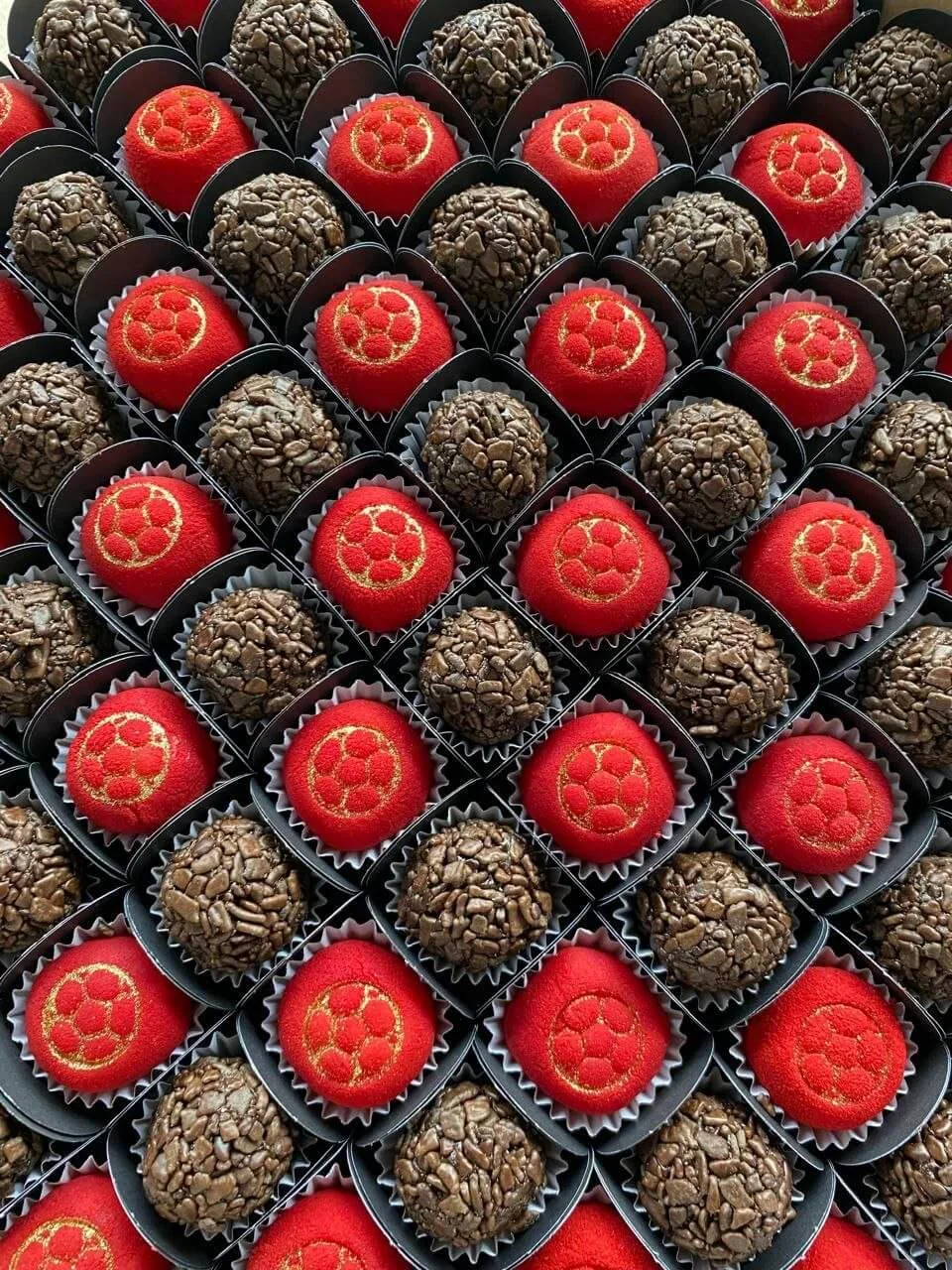 Docinhos temáticos vermelhos com carimbo dourado ao lado de brigadeiros de granulado