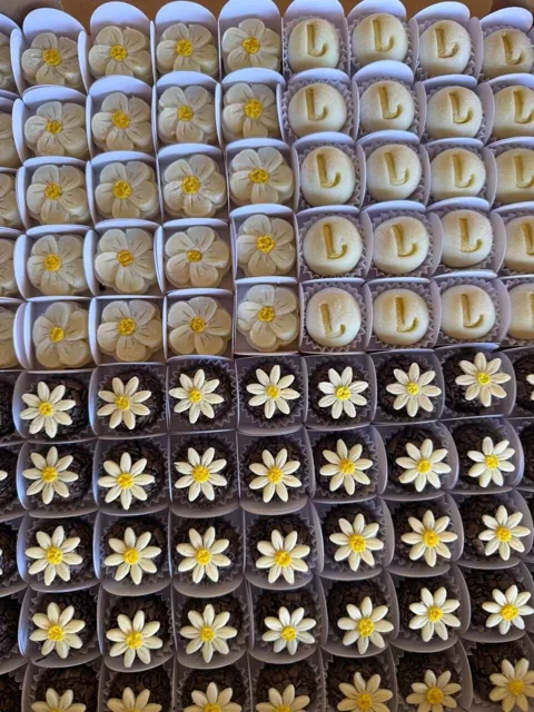 Docinhos modelados em formato de flor e da letra L, e brigadeiros com margaridas de chocolate branco