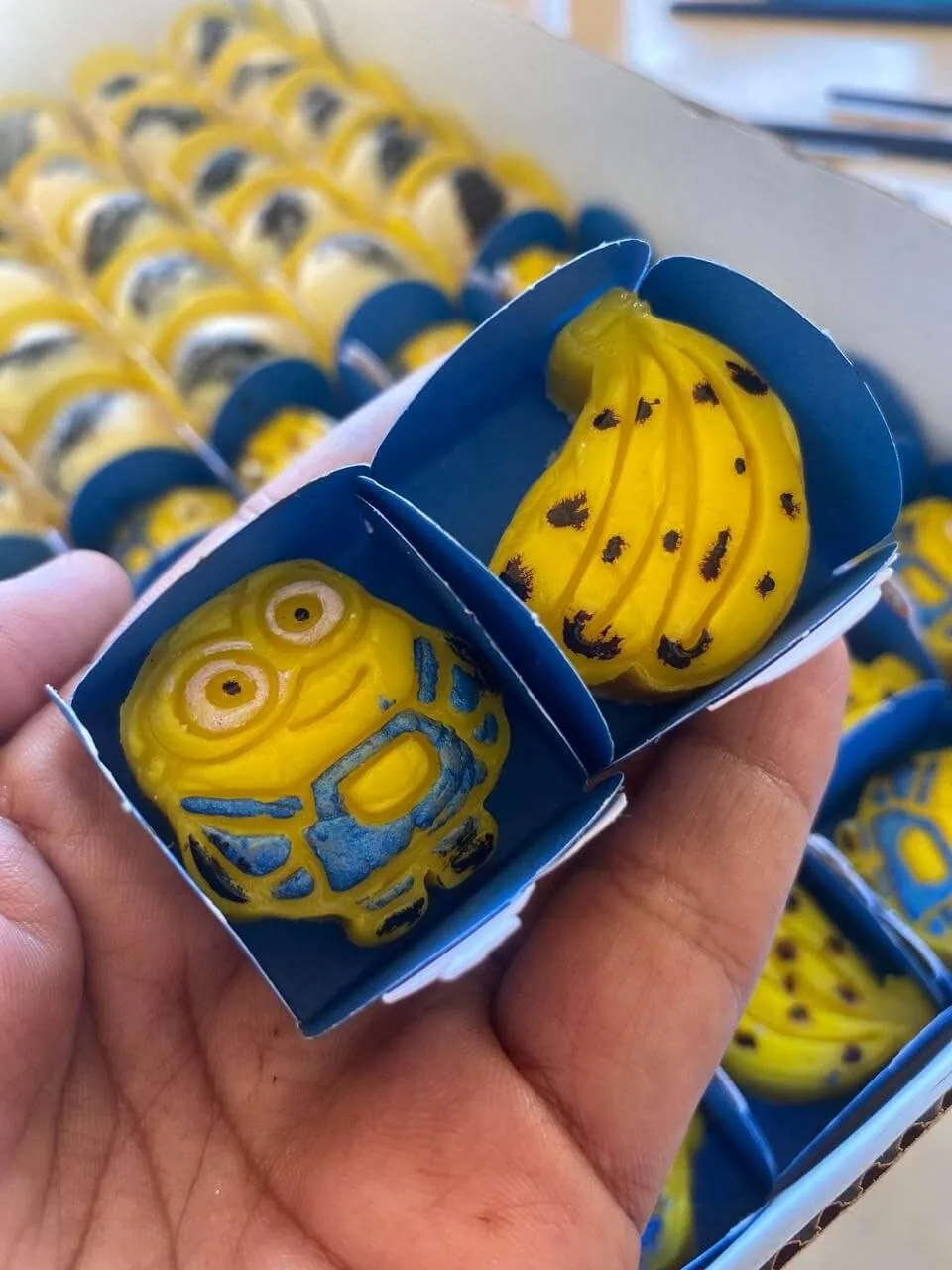 Docinhos modelados em formato de Minion e de cacho de bananas, em caixinhas azuis